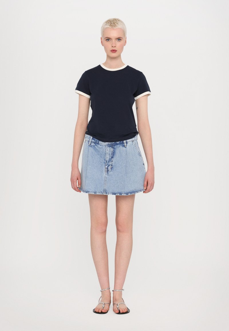 Marineblaues T-Shirt mit weißem Besatz, kombiniert mit einem hellblauen Jeansrock. Das Model trägt silberne Sandalen. Einfaches, lässiges Outfit mit lockerer Passform.