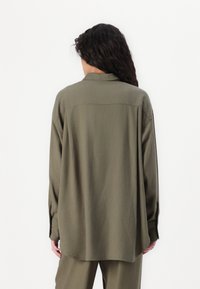 Camisa verde de manga longa com colarinho, corte descontraído e yoke nas costas. Textura suave com punho abotoado e bainha arredondada.