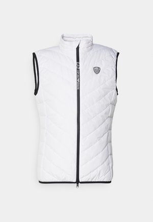 Bijela bezrukavna puffer prsluk s visokim vratom, dijamantnim štepom, crnim patent zatvaračem i suptilnim logom na prsima.