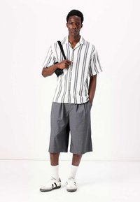 Camisa de manga corta con botones, de rayas blancas y azul marino, pantalones cortos grises hasta la rodilla, calcetines blancos y zapatillas con rayas negras.