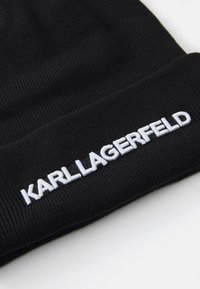 Gorro de punto negro con textura acanalada que presenta el logo bordado en blanco "KARL LAGERFELD" en el dobladillo delantero.
