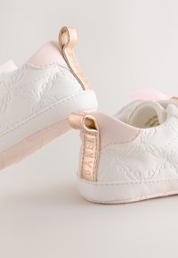 Witte lederen sneakers met roze accenten, geperste bloemmotieven en een gouden metalen achterkant met het label "BAKER." Heeft een zachte textuur en een afgeronde vorm.