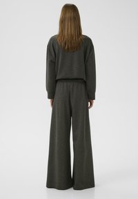 Ensemble en tissu doux comprenant un sweat-shirt oversized gris foncé et un pantalon large. Le haut présente des épaules basses et une coupe décontractée.