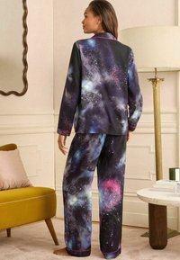 Fekete pizsama szett, galaxis mintával kék, lila és rózsaszín árnyalatokban. Rózsaszín díszítéssel. Simaságot adó anyag, laza szabás.