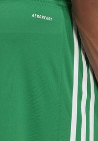 Groene sportshorts van textiel met een gestructureerde stof, voorzien van witte strepen aan de zijkanten en een "AEROREADY" logo op de taille.