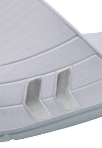 Vit gummisula till sneakers med strukturerat vågmönster, med silverdetaljer och vinklade utskärningar, designad för grepp och flexibilitet.