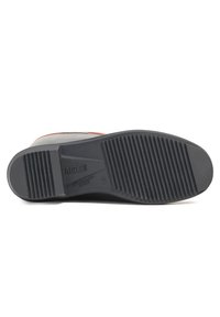 Semelle de botte en caoutchouc noire avec des motifs de crampons horizontaux et verticaux ; présente le logo de la marque et du texte en relief sur le côté.