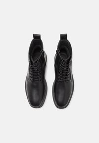 Bottines en cuir noir avec une texture lisse, dotées de lacets, d'une fermeture éclair latérale et de poignées pour un enfilage facile. Design à bout rond.