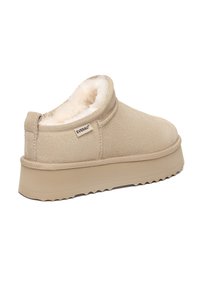 Beige Wildleder Slippers mit weichem Innenfutter, dicker Gummisohle und gezacktem Rand. "EVERAU"-Logo an der Seite.