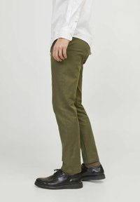 Olive green cotton pants with a slim fit, featuring side seams and a slightly tapered leg, paired with black leather shoes.
