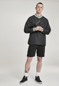 Svart langermet topp med en fargerik stripet krage, sammen med svarte shorts. Svarte joggesko og hvite sokker fullfører antrekket.