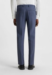 Pantaloni sartoriali blu navy con texture liscia, dotati di doppie tasche posteriori e vestibilità slim. Abbinati a scarpe formali nere.