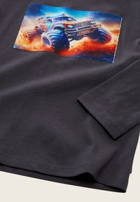 Dunkelblaues Langarmshirt mit einem bunten Grafik eines Monstertrucks, der springt und Staub aufwirbelt vor einem blau-orangen Himmel.