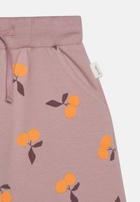 Lys rosa joggebukser laget av bomull, med et mønster av appelsiner og blader. Elastisk liv med snor og sidelommer.