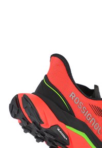 Zapatilla roja y negra con parte superior de malla, que presenta una suela texturizada, acentos en verde neón y la marca "ROSSIGNOL" en el lateral.
