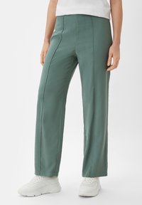 Green wide-leg trousers with a smooth texture, featuring front seams and a high waist, paired with white sneakers.