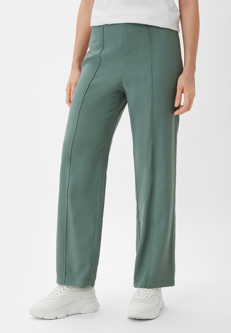 Green wide-leg trousers with a smooth texture, featuring front seams and a high waist, paired with white sneakers.