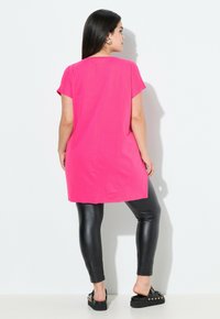 Fuchsia oversized t-shirt met korte mouwen, zachte textuur en rechte snit, gecombineerd met zwarte neplederen leggings en platform sandalen.