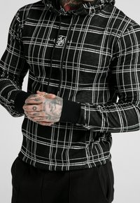 Black and white plaid hoodie with a drawstring, featuring a comfortable fit and ribbed cuffs. Textured fabric with a subtle sheen.