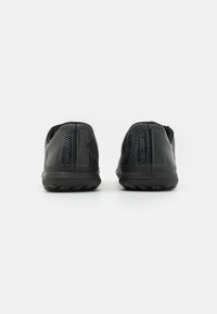Zapatillas deportivas negras con parte superior de malla texturada, que presentan un patrón estriado y suelas de goma con tacos de tracción. Diseño ligero.