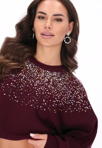 Bordeaux trui met een cropped ontwerp, versierd met pailletten in gouden en zilveren tinten, met ribbeltjesstructuur en ronde halslijn.