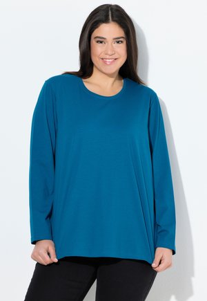 Haut à manches longues teal avec un col rond, en tissu doux, coupe décontractée, associé à un pantalon noir, présenté sur un fond blanc.