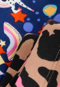Des textiles avec un fond bleu foncé orné de motifs colorés, comprenant des étoiles, des points, des arcs-en-ciel et des impressions animales en marron et rose.