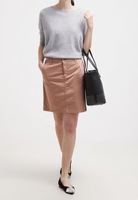 Maglione grigio a maglia, gonna beige fino al ginocchio, borsa nera con dettagli borchiati e ballerine nere con punte d'argento.