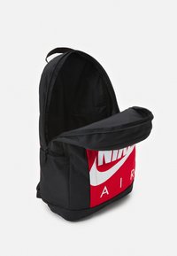 Svart tygryggsäck med en röd frontpanel, som har en stor vit Nike Air-logotyp, zippered öppning och sidoficka.