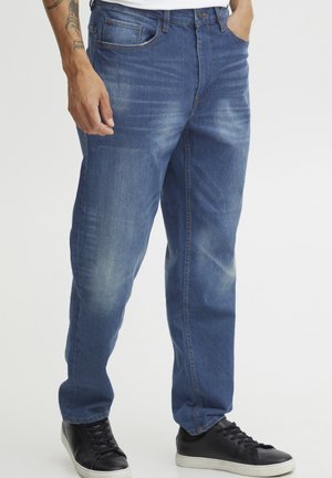 Blue denim jeans with a relaxed fit, featuring subtle fading, five-pocket design, and standard waistband. Paired with black sneakers.