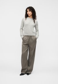 Pull gris en matière douce, associé à un pantalon ample marron clair. Des chaussures noires à bout pointu complètent la tenue.