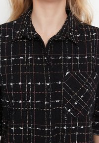 Camicia a maniche lunghe con motivo a scacchi neri realizzata in tessuto testurizzato, con motivi in filo bianco e colorato, colletto a punta e dettaglio della tasca sul petto.