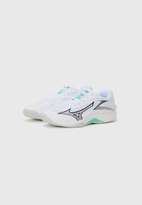 White athletic shoes with mesh upper, black and green accents, and textured sole for grip. Features prominent logo design on the side.
