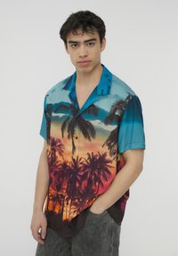Camicia a maniche corte con bottoni, caratterizzata da una sfumatura di blu all'arancione del tramonto con silhouette di palme. Realizzata in tessuto leggero e morbido.