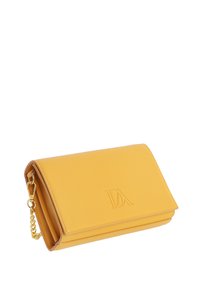 Clutch de cuero amarillo con una correa de cadena dorada y las iniciales “IDA” en relieve en la solapa, en ángulo sobre un fondo blanco.