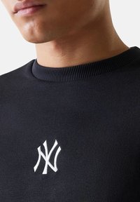 Felpa nera con scollo girocollo a costine e logo ricamato bianco sul petto. Texture liscia, design aderente.