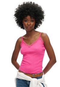 Top rosa ajustado con textura acanalada, borde de encaje a lo largo del escote en V, tirantes finos, llevado con una camisa blanca alrededor de la cintura.