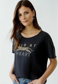 Black soft fabric t-shirt with a relaxed fit, featuring a gold and animal-print graphic that reads "WILD AT HEART." Short sleeves, round neckline.