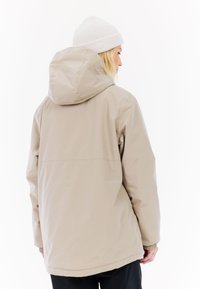 Beige wasserfeste Jacke mit Kapuze, elastischen Bündchen und lässigem Schnitt. Hergestellt aus leichtem, glattem Material. Einfaches Design, keine auffälligen Muster.