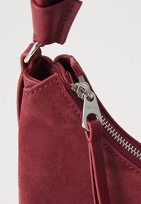 A close-up of a red suede handbag featuring a silver zipper and a strap, highlighting its soft texture and stylish design.