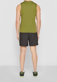 Haut vert sans manches avec un col rond, associé à un short de sport noir et des baskets noires avec des accents verts.