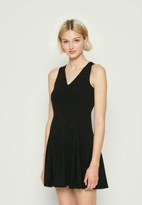 Vestido preto sem mangas com um decote em V, corpete justo e saia plissada. Feito de um tecido suave com uma textura leve.