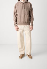 Brun huvtröja med ficka fram, tillsammans med löst sittande krämfärgade byxor och ljusbruna mockaskor. Strukturerad tyg överallt.