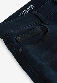 Jeans de mezclilla azul oscuro con una etiqueta de "Comfort Stretch", que presentan un bolsillo frontal, detalles de botones y costuras visibles a lo largo de las costuras.