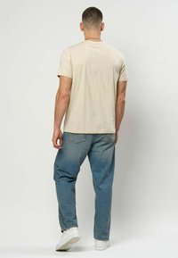 Beige t-skjorte med korte ermer kombinert med lyseblå jeans. T-skjorten er laget av mykt stoff; jeansene har en avslappet passform og en falmet struktur.