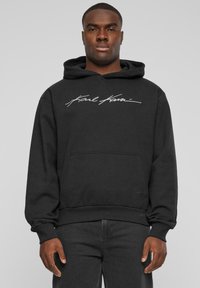 Sudadera con capucha negra hecha de mezcla de algodón. Presenta un logo bordado blanco en el pecho, bolsillo tipo canguro y puños y dobladillo acanalados.