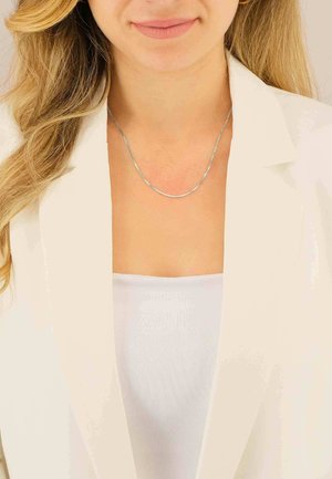 Collana in argento con una superficie liscia e sottile, caratterizzata da un design delicato e arrotondato che si adagia lungo la clavicola.