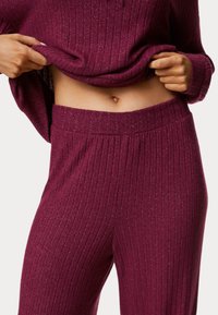 Burgundy ribbed knit top and pants set with metallic sheen; features a wide waistband and textured fabric. Smooth, fitted silhouette.