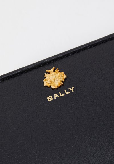 Monedero de piel negra que presenta una superficie texturizada, emblema dorado con detalles intrincados y el nombre "BALLY" grabado en dorado debajo.