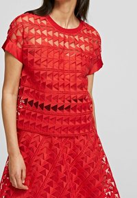 Top rojo de manga corta con un patrón geométrico de triángulos recortados. Fabricado con un tejido ligero y texturizado, con escote redondo.